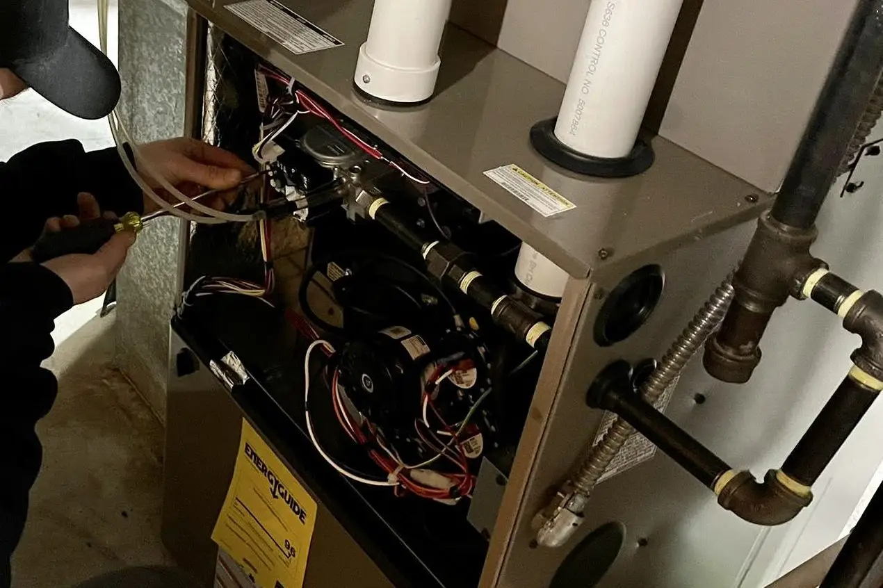 Technician servicing the controls inside an open gas furnace cabinet