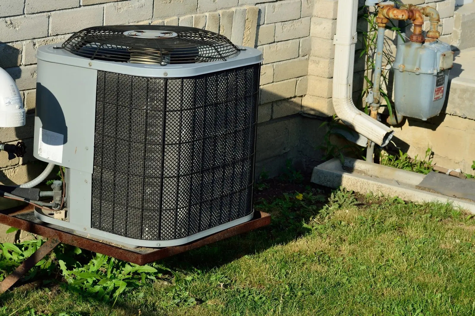 Central air conditioner condenser beside a block wall house next to the gas meter