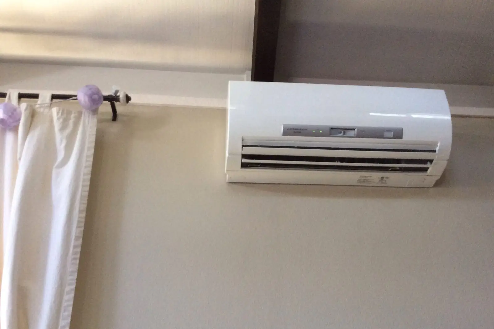 Ductless mini split indoor unit mounted high on a bedroom wall