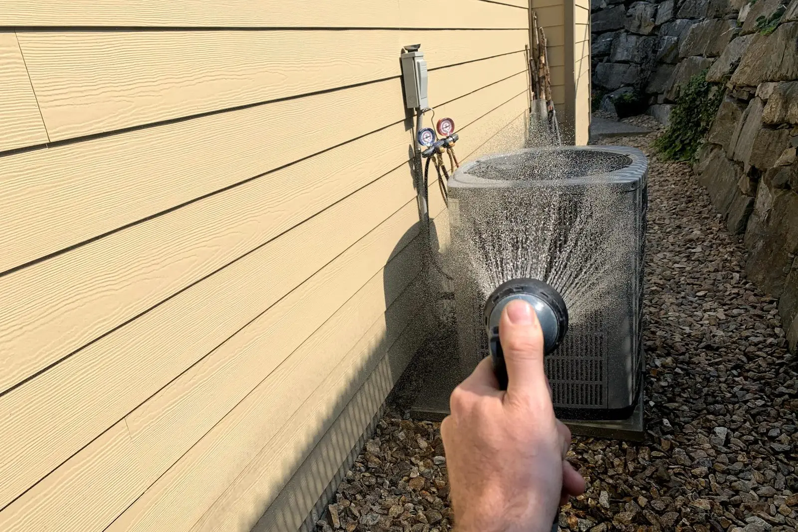 Rinsing an outdoor AC condenser coil with a garden hose during a maintenance visit