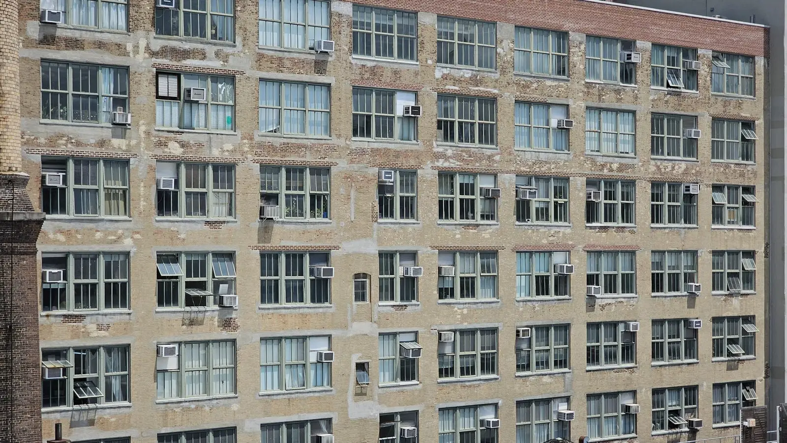 Older brick building facade with window air conditioners in many windows